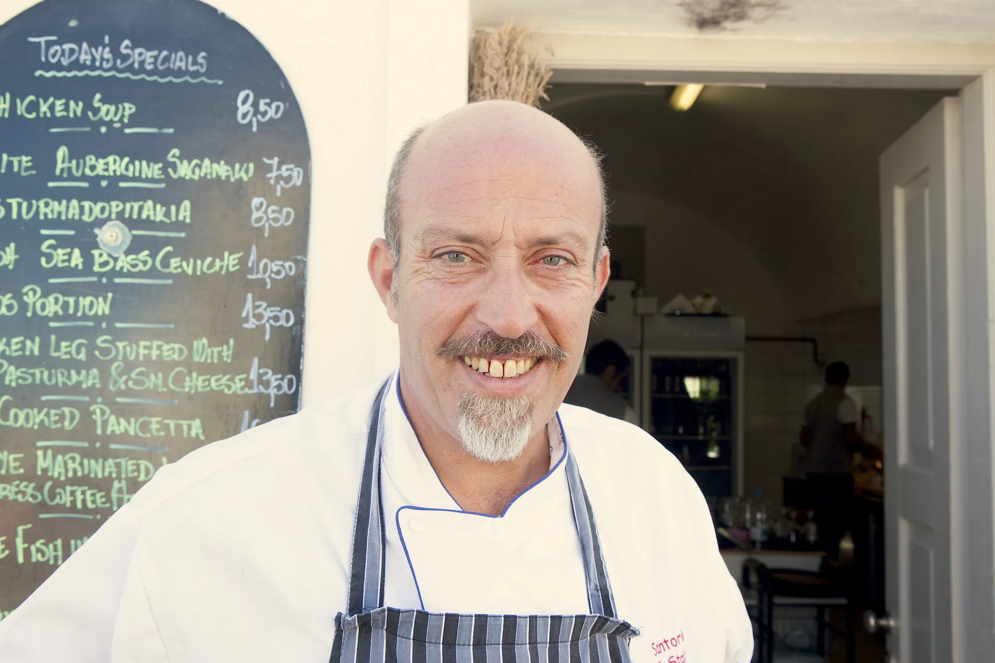Chef Giorgios smiling in front of the chalkboard of today’s specials