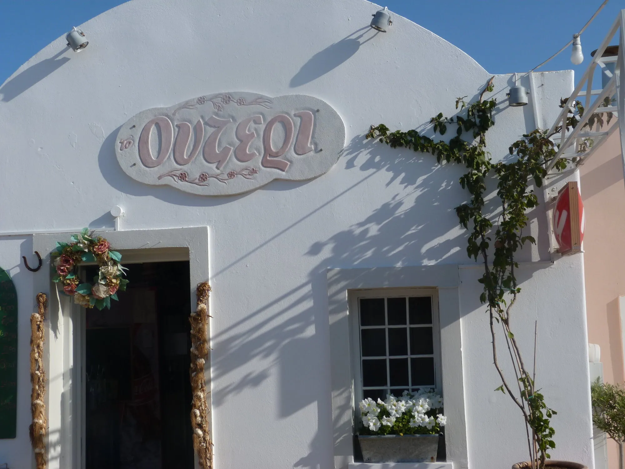 The whitewashed entrance with the hand-painted Ouzeri sign